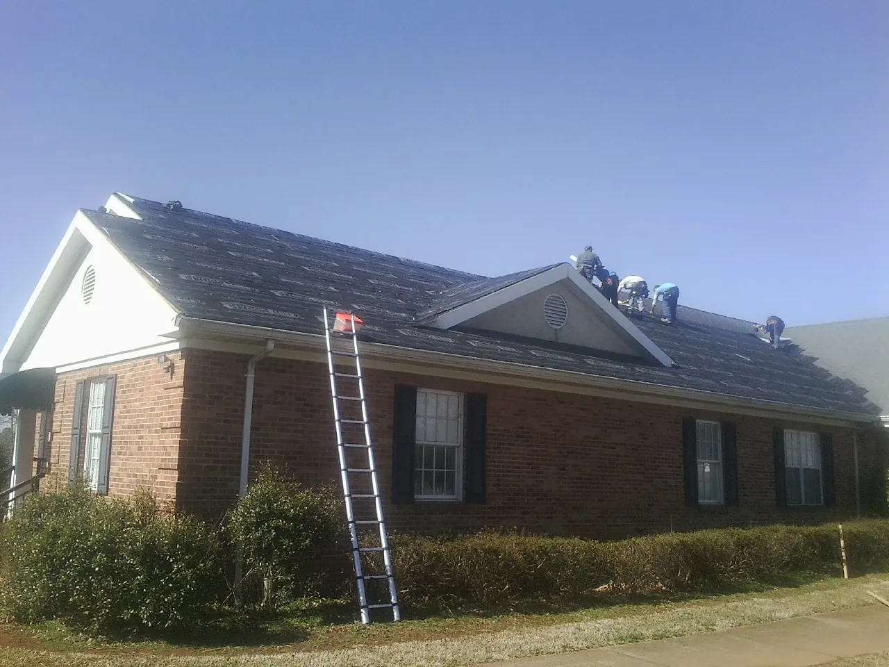 Crew tearing shingles off a brick ranch roof with a ladder set — Emergency Roof Repair work by our crew in Severna Park