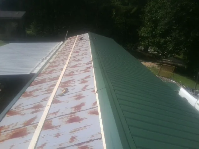 Old rusted panels beside newly installed green metal roofing — Wind Damage Roof Repair by Roofing Brothers in Severna Park