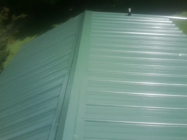New green metal panels meeting at the ridge of a roof — Flat Roof Repair work by our crew in Severna Park