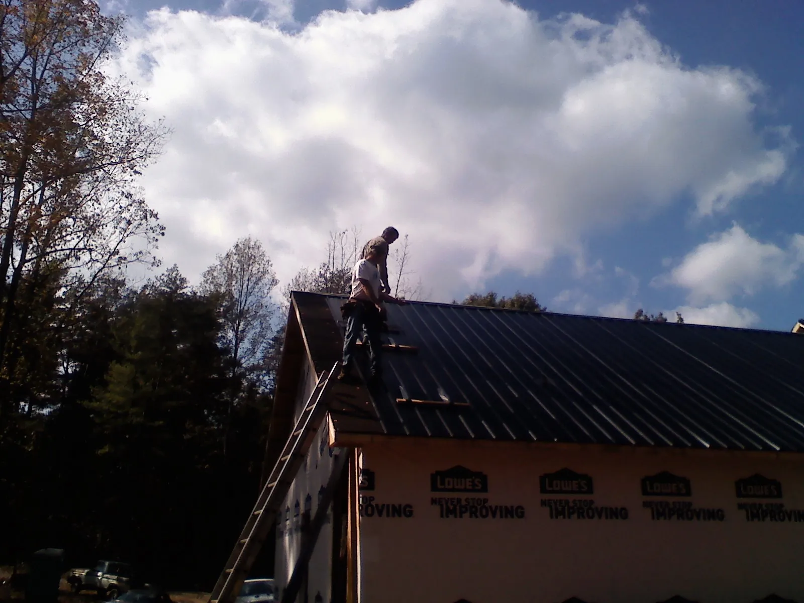 Roofer fastening dark metal panels high against a cloudy sky, from a Roof Inspection job in Severna Park
