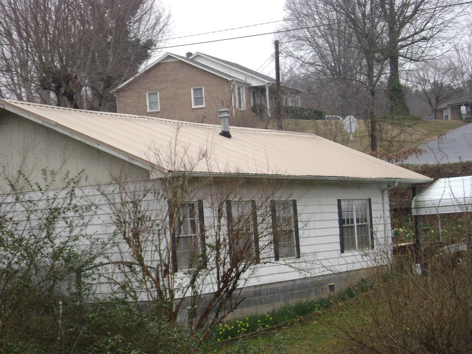 Tan metal roof on a white sided house set into a hillside — Commercial Roofing by Roofing Brothers in Severna Park